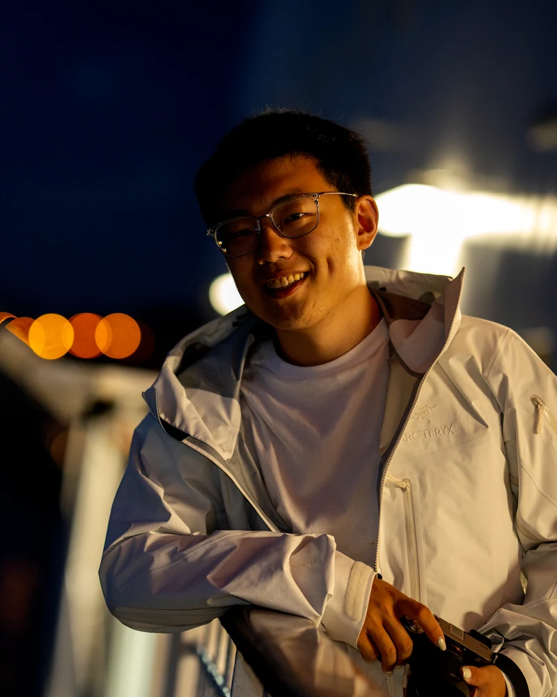 Qianxu holding a camera beside the water at night